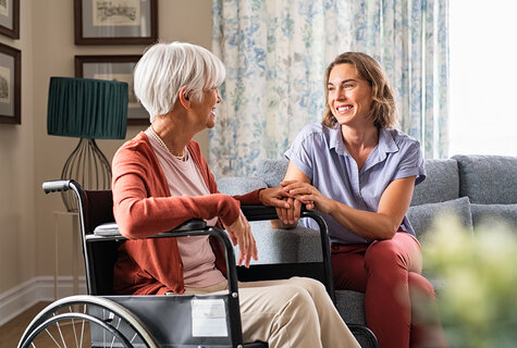 Seniorin im Rollstuhl, Pflegerin hält ihre Hand
